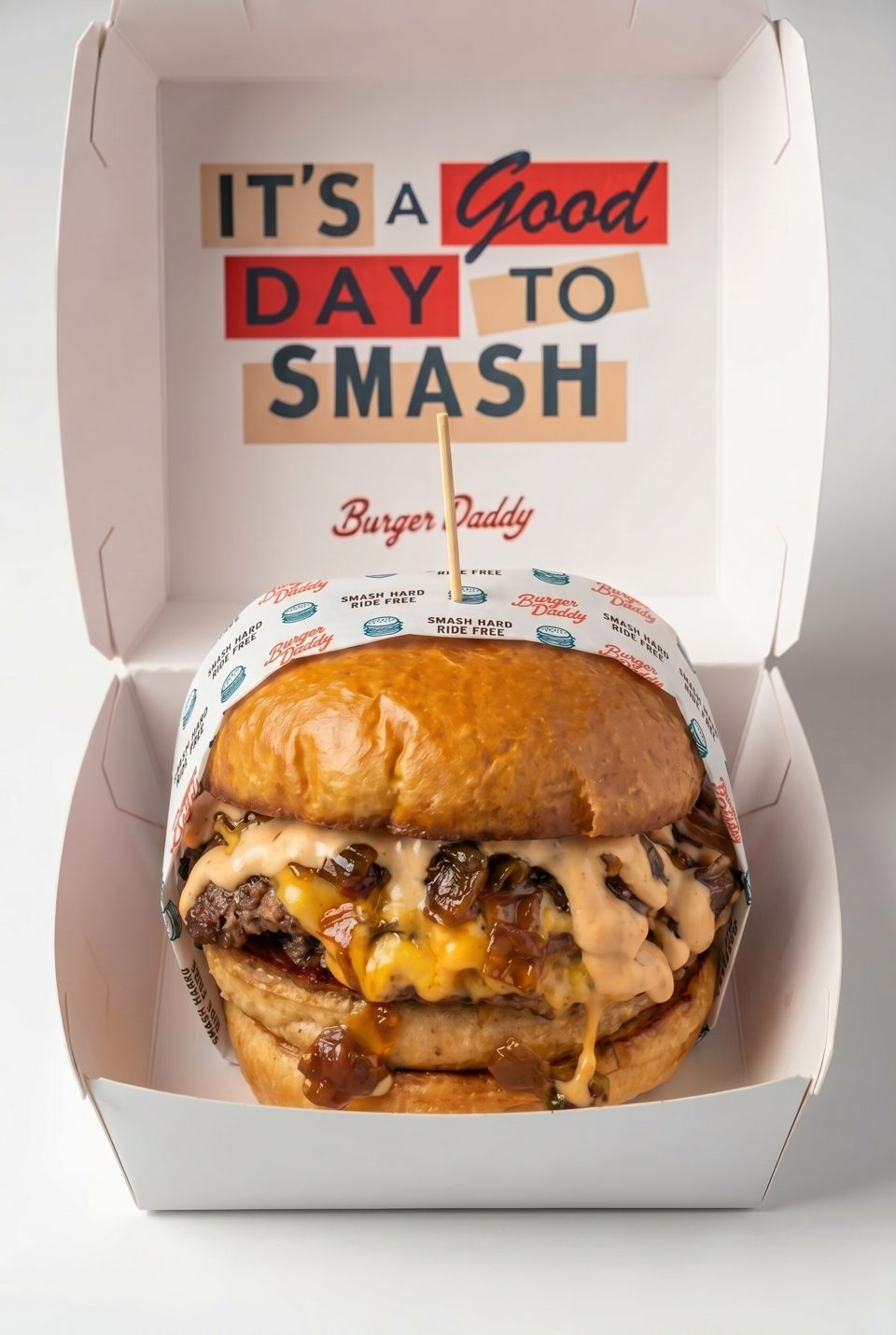 A Burger Daddy smash burger with cheese and caramelized onions in a white takeout box.